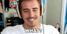 a man wearing headphones and a white shirt is smiling and asking what .