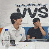 two men sit at a table with a sign that says vvs