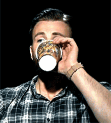 a man wearing a plaid shirt is drinking from a paper cup