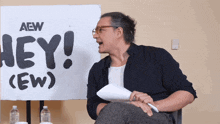 a man sitting in front of a sign that says hey ew