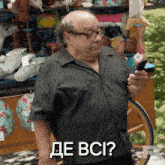 a bald man with glasses is holding a cell phone in front of a cart full of stuffed animals and says de bci