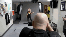 a bald man is taking a picture of a woman in front of a camera