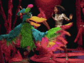 a woman is dancing in front of a colorful bird
