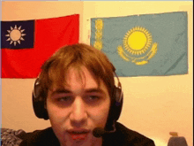 a man wearing headphones and a microphone stands in front of a taiwan flag and a kazakh flag