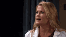 a woman in a white lab coat is standing in front of a black curtain and looking up .