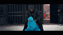 a man in a black jacket is riding a blue inflatable hippopotamus