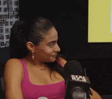 a woman in a pink tank top is sitting in front of a real 92.3 microphone