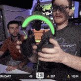 a man wearing a raidart shirt is holding a controller in front of a microphone