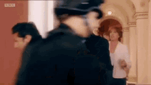 a group of people are walking down a hallway with a police officer in the foreground and a woman in the background .