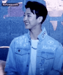 a young man wearing a blue denim jacket and a white t-shirt is smiling .