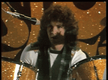 a man with a scarf around his neck is playing drums on a stage