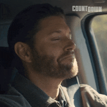 a man with a beard is sitting in a car with his eyes closed and the word countdown behind him