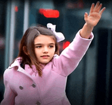a little girl in a pink coat is waving