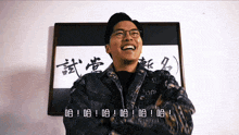 a man wearing glasses and a denim jacket is laughing in front of a picture with chinese writing on it