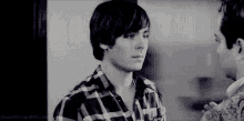 a black and white photo of a man in a plaid shirt standing next to another man .