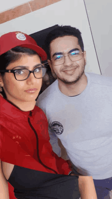 a man and a woman are posing for a picture and the woman is wearing a red jacket with the letter x on it