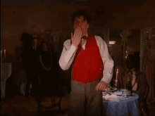 a man in a red vest is standing in front of a table with a bottle of wine on it