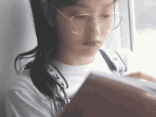 a young woman wearing glasses is reading a book .