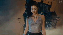 a woman in a silver top and black pants is standing in front of a painting .