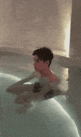 a young man is sitting in a swimming pool without a shirt on