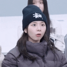 a woman wearing a black beanie and a gray jacket is sitting in a classroom .