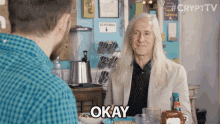 a man with long hair says okay while sitting at a table with other people