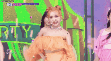 a woman in an orange dress is standing in front of a green sign that says the show