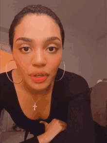 a woman wearing hoop earrings and a cross necklace looks at the camera
