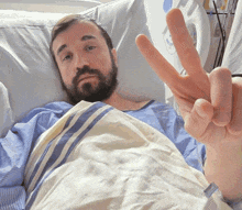a man with a beard is laying in a hospital bed and giving a peace sign