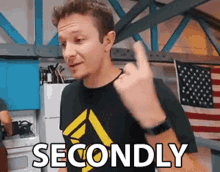 a man in a black shirt is giving the middle finger and the word secondly is behind him .
