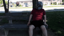 a man wearing a bounty hunter mask sits on a bench