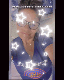 a woman wearing glasses and a nyc rhythm shirt is taking a selfie .
