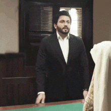 a man in a suit and white shirt is standing in front of a desk .