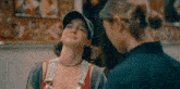 two women are standing next to each other and one of them is wearing a hat and overalls .