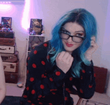 a woman with blue hair is wearing glasses and a black polka dot shirt