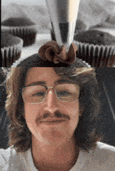 a man with glasses and a mustache looks at a cupcake