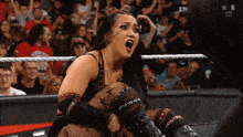 a woman in a wrestling ring is screaming in front of a crowd that is watching a live show