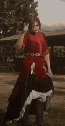 a woman in a red dress and black skirt is standing on a dirt field in a video game .