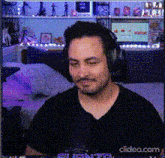 a man wearing headphones and a black shirt is sitting in front of a microphone in a room ..