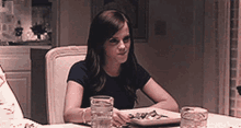 a woman is sitting at a table with a plate of food and glasses of water