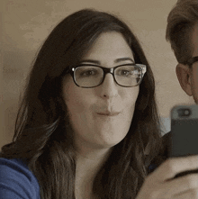 a woman wearing glasses is blowing a kiss while looking at her phone