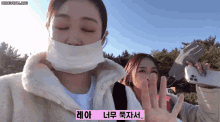 a woman wearing a mask holds up her hand in front of another woman who is holding a cell phone