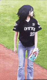 a woman in a baseball uniform is standing on a baseball field holding a baseball glove .