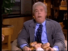 a man in a suit and tie is sitting in a chair eating a bunch of donuts .