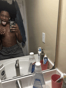 a man taking a picture of himself in a bathroom mirror with a bottle of aquafina toothpaste on the sink