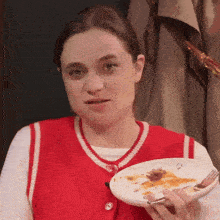 a woman wearing a red vest is holding a plate of food
