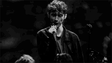 a black and white photo of a man singing into a microphone on stage .