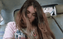 a woman with long hair is sitting in the back seat of a car with her eyes closed .