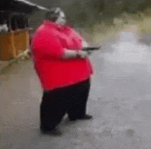 a fat man in a red shirt is holding a gun and wearing headphones .