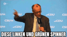 a man in a suit and tie is standing in front of a microphone with the words diese linken und grünen spinner above him